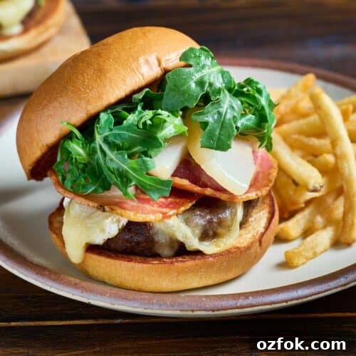Hamburger topped with melted brie cheese, poached pears, crispy pancetta and fresh arugula on a brioche bun served on a plate