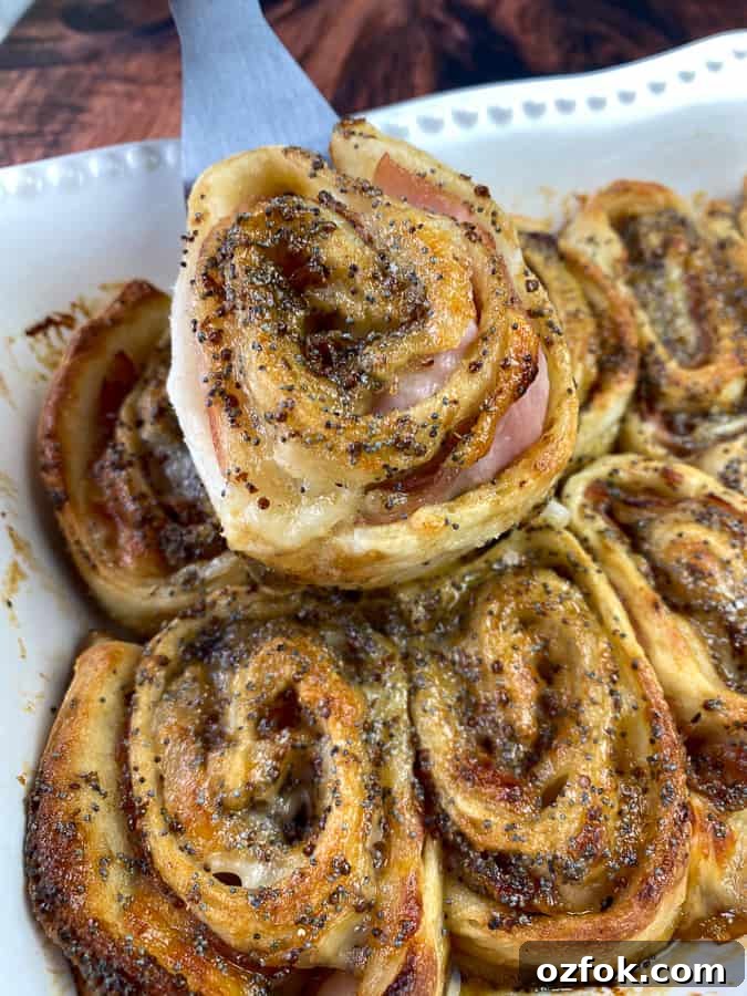 Ham and cheese pinwheel on serving spatula above pan full of pinwheels