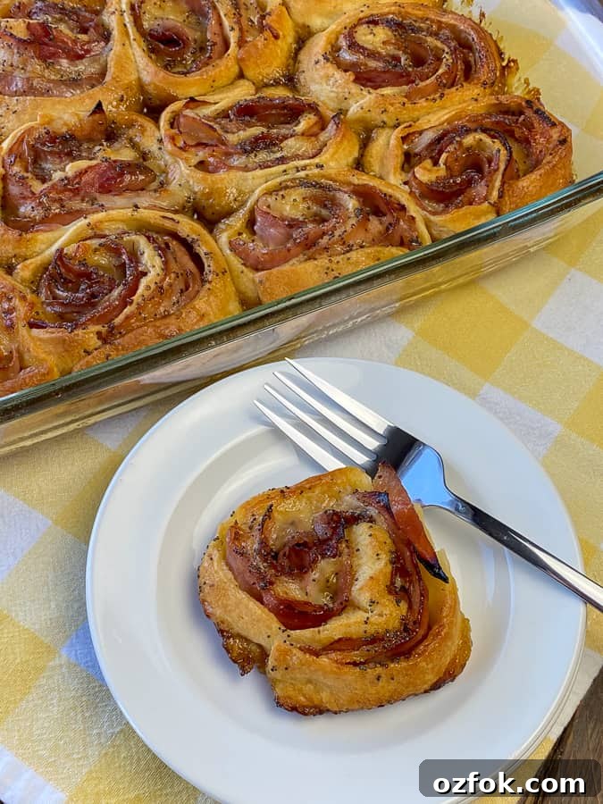 Ham Roll-up on white plate with fork next to full baking dish on yellow plaid napkin