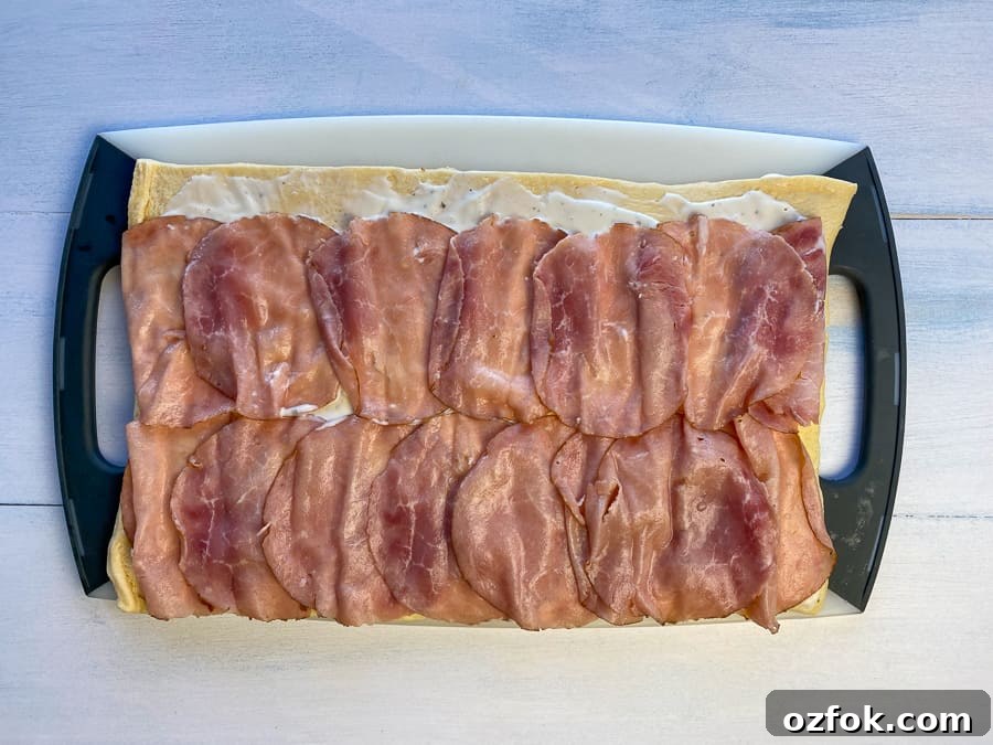 Crescent dough on cutting board with ranch dressing and layer of ham lunchmeat