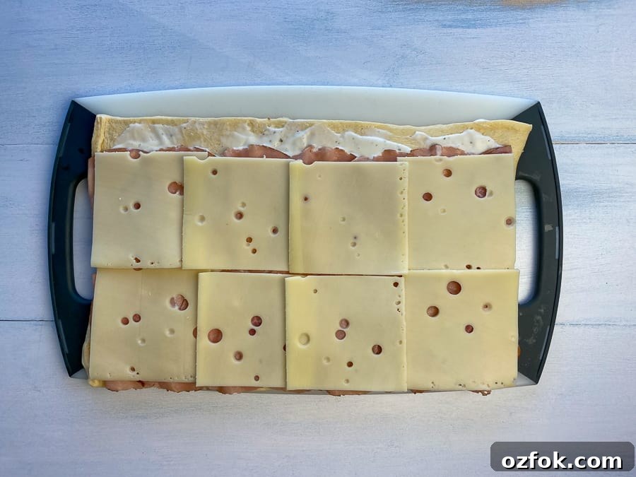 Layer of sliced Swiss cheese added on top of ham roll-up