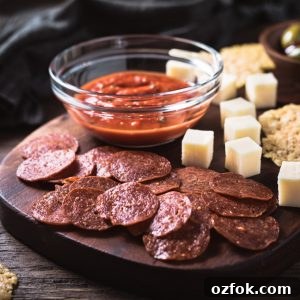 Keto Parmesan Crisps: Crispy Low-Carb Cheese Chips 6 Pepperoni chips, cheese cubes, and Marinara sauce on a cutting board.