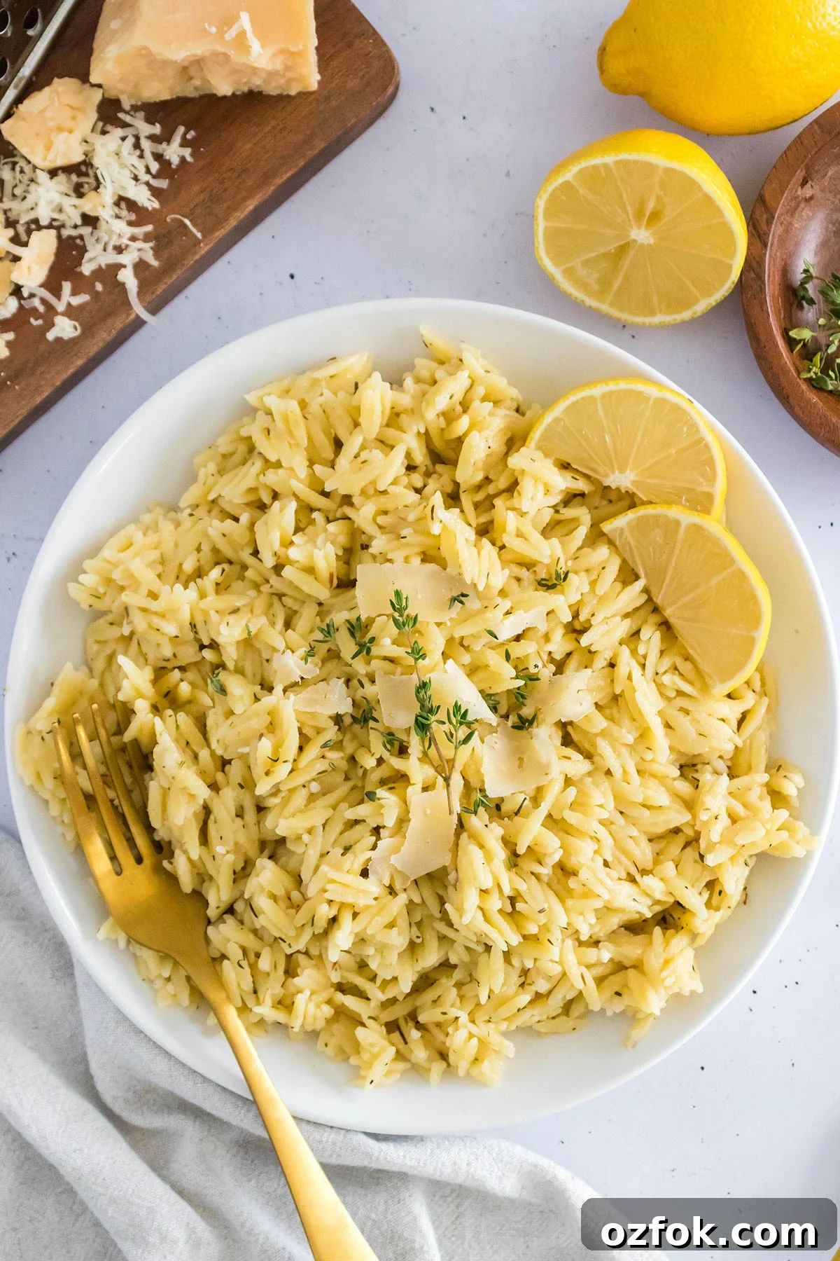 Zesty Lemon Orzo with Parmesan and Fresh Herbs 5 Lemon Orzo pasta served on white plate with lemon slice and a fork.