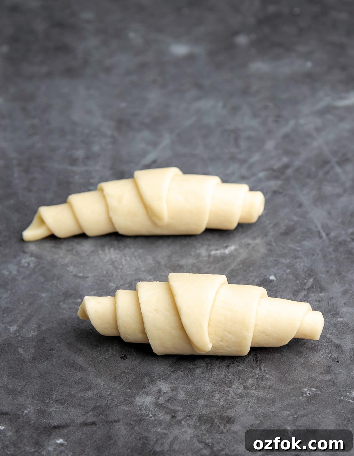 Flaky Gluten-Free Croissants: Buttery Recipe for Perfect Layers 7 Two raw shaped gluten free croissants on gray background