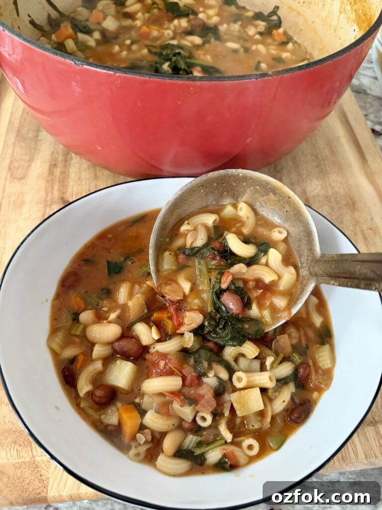 Classic Italian Minestrone Soup Recipe — Hearty Vegetable Stew 12 Pouring Italian minestrone soup into white bowl with ladle from large Dutch oven full of soup in background.