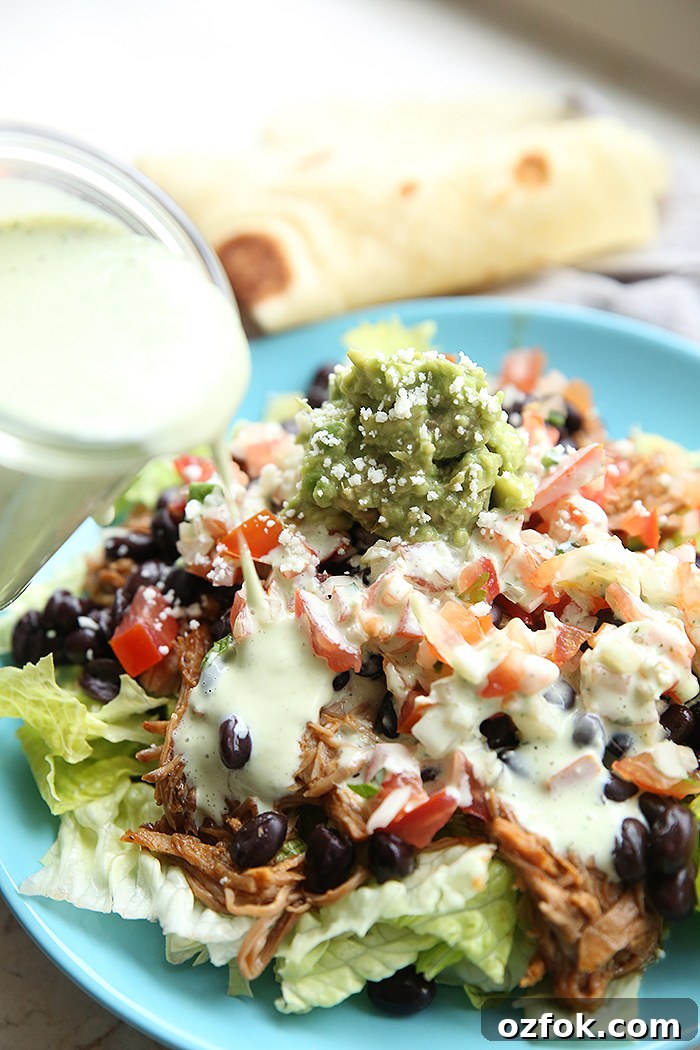 Cafe Rio Shredded Chicken Copycat Recipe That Tastes Like the Original 2 A light blue dinner plate with chopped lettuce topped with shredded chicken black beans, pico de Gallo, and guacamole being drizzled with dressing from a tilted bottle on the left. Faded in the background is a folded tortilla.