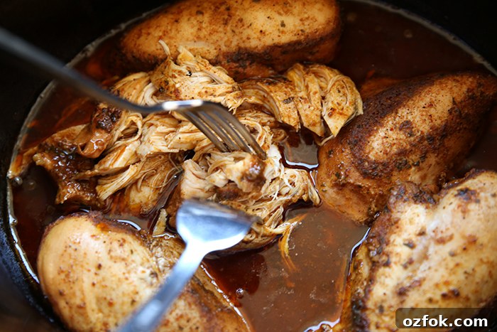 A crockpot of cafe rio chicken breasts with two forks inserted into a partially shredded chicken breast.