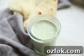 A jar of cilantro ranch dressing next to a grey napkin with a folded flour tortilla sitting on top of the napkin.