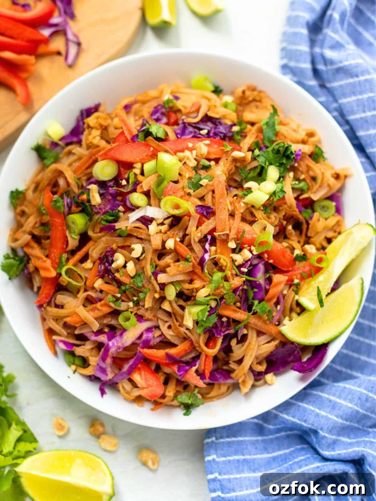 Thai Noodles Bowl filled with Thai noodles tossed with peanut sauce and fresh vegetables next to fresh limes and peanuts.