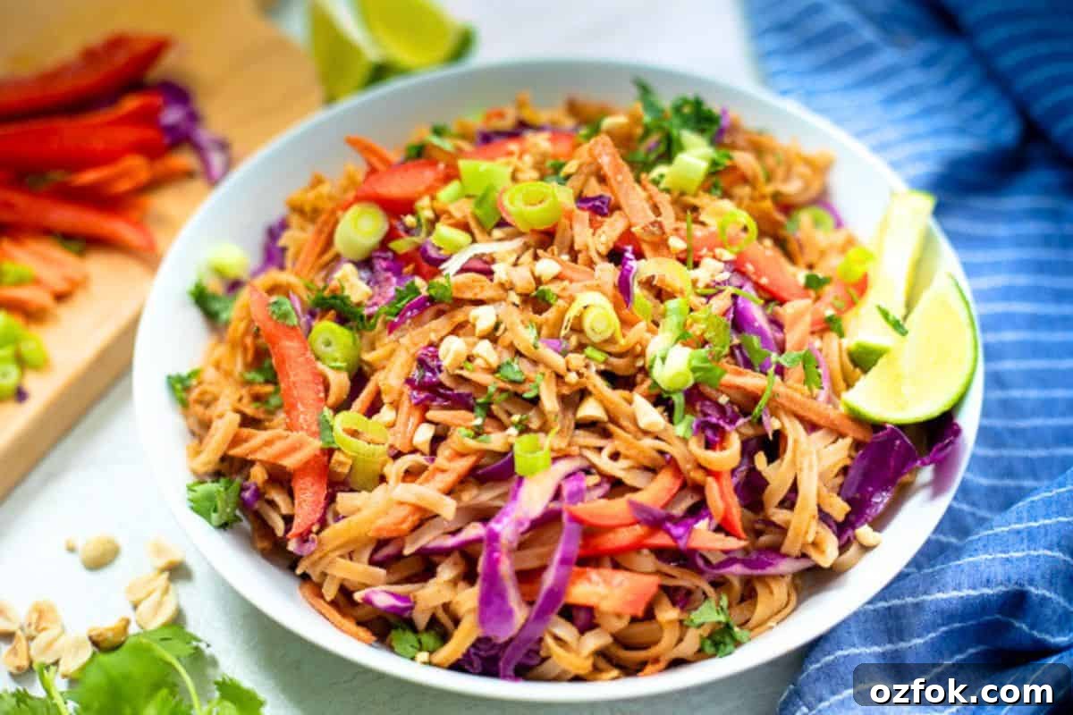 Thai Noodles with Homemade Peanut Sauce Bowl filled with Thai noodles tossed with peanut sauce and fresh vegetables next to fresh limes, cilantro, green onions, and peanuts.