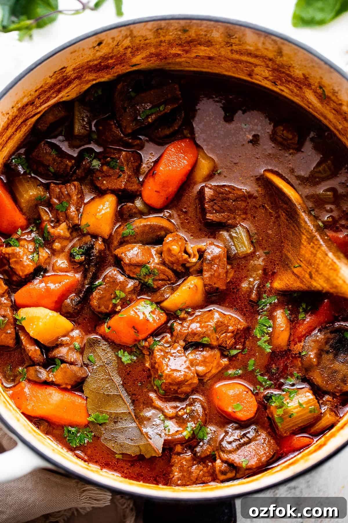 This hearty, Irish inspired Guinness Beef Stew is packed with tender beef, potatoes, carrots, and mushrooms, all cooked in a thick, delicious savory broth. overhead shot of a white dutch oven filled with guinness beef stew.