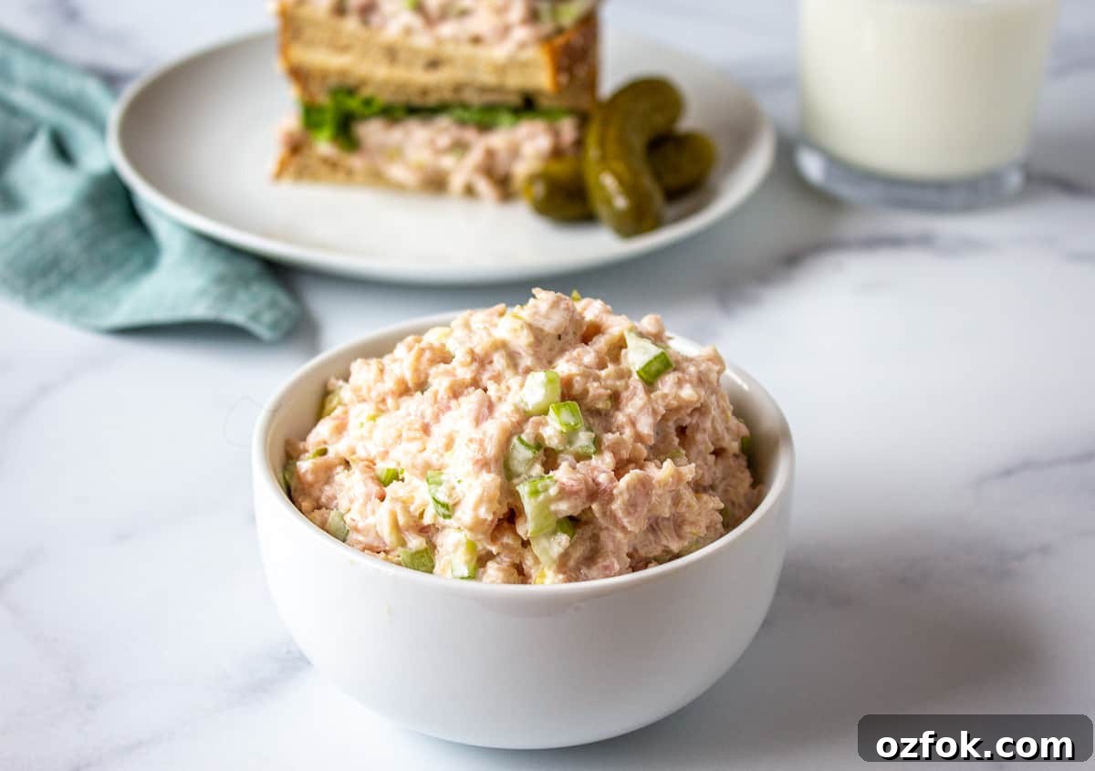 Classic Creamy Ham Salad Recipe for Sandwiches and Dips 7 A small white bowl filled with a ham salad and a sandwich in the background.