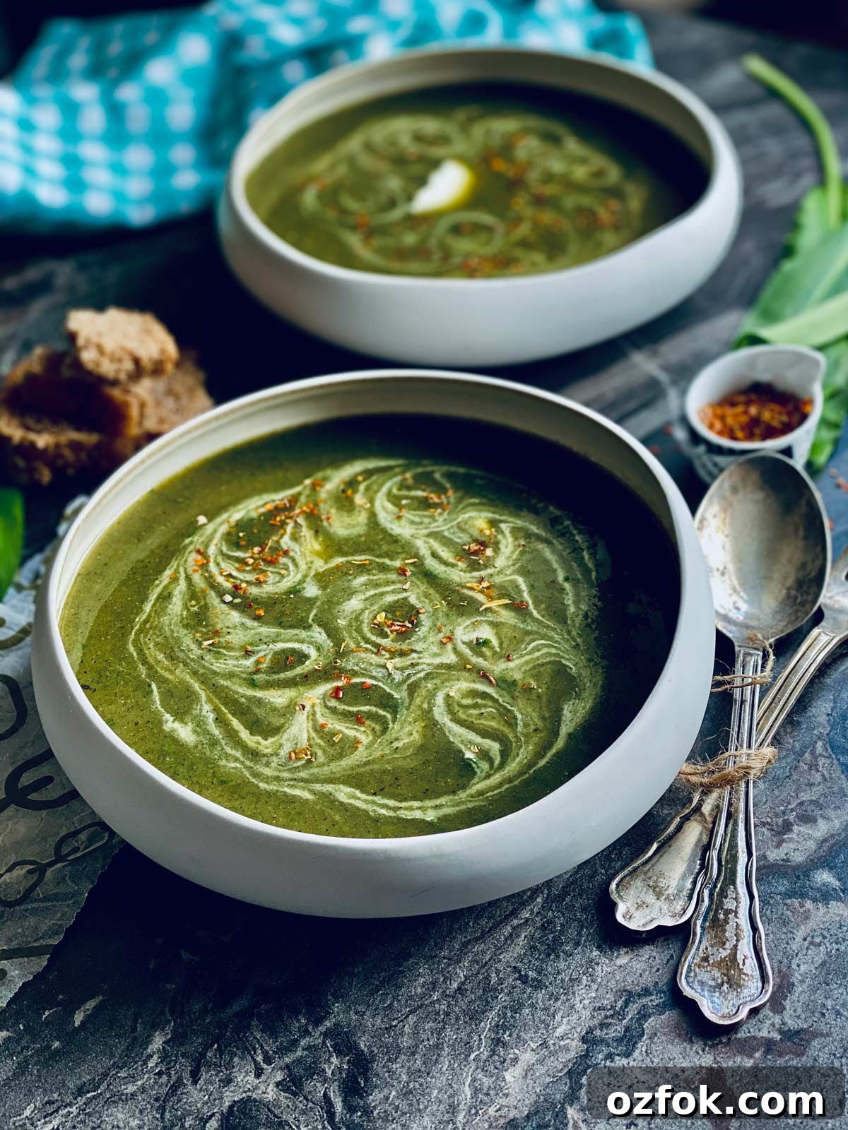 Wild Garlic and Nettle Soup Recipe: Creamy Spring Foraging Bowl 2 Two white bowls with wild garlic and nettles soup with cream swirls and red chilli flakes sprinkled on top on a marbled worktop