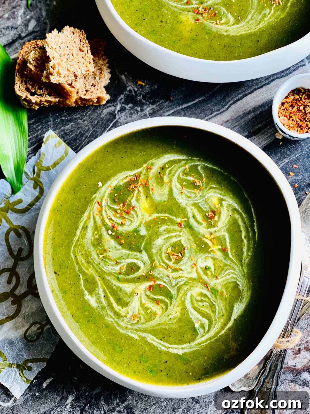 Wild Garlic and Nettle Soup Recipe: Creamy Spring Foraging Bowl 6 Freshly foraged wild garlic soup in a white presentable soup bowl birds-eye view with swirled up cream and a pinch of chilli flakes on a dark black marble worktop