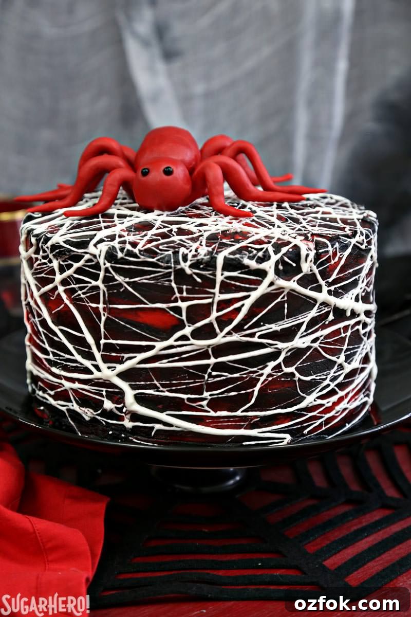 Red Velvet Marshmallow Spiderweb Cake—classic red velvet cake with black chocolate buttercream, covered with a web of marshmallow spiderwebs! Red Velvet Marshmallow Spiderweb Cake with red candy spider on top