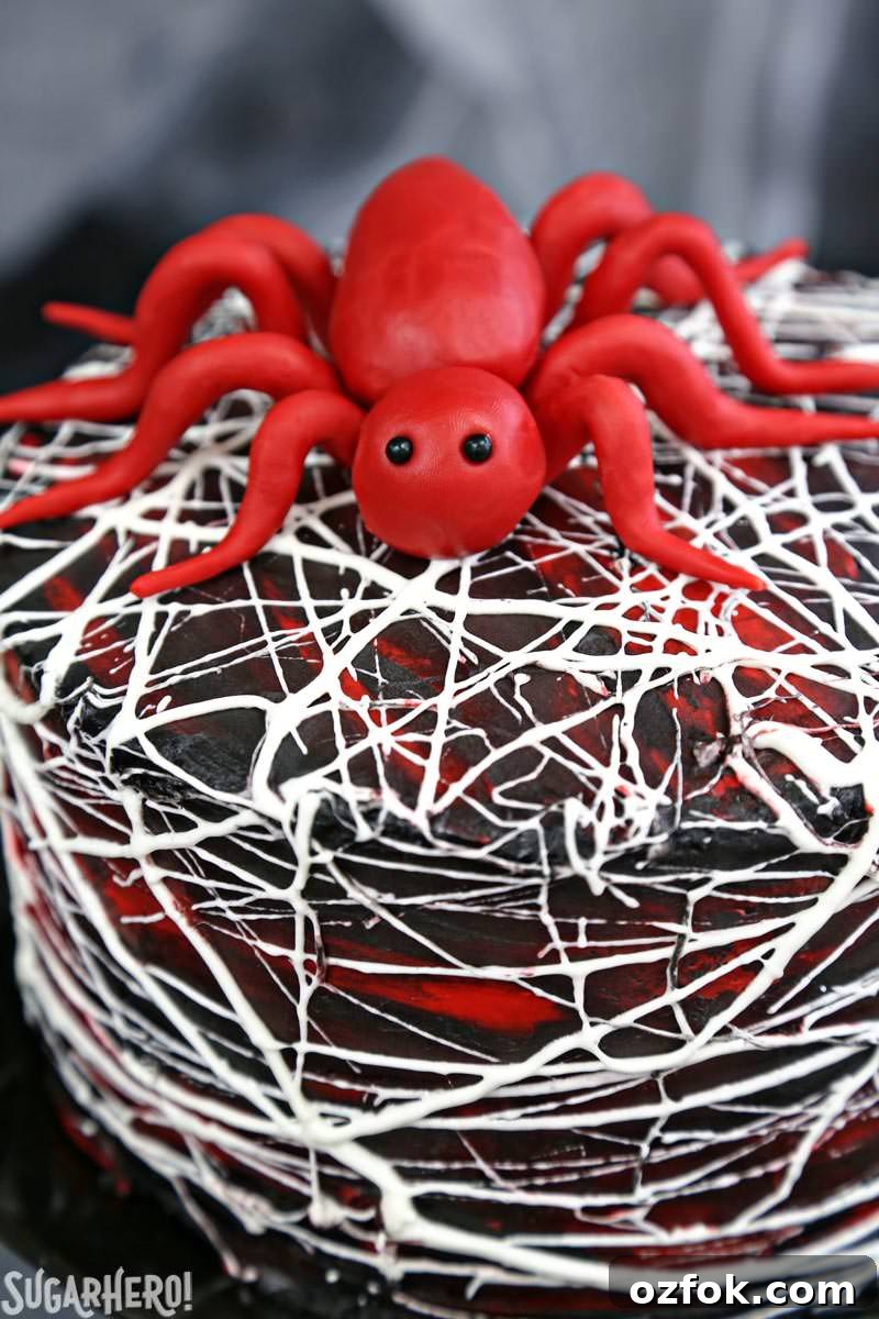 Red Velvet Marshmallow Spiderweb Cake—classic red velvet cake with black chocolate buttercream, covered with a web of marshmallow spiderwebs! Red Velvet Marshmallow Spiderweb Cake - red candy spider on top of marshmallow web-covered cake