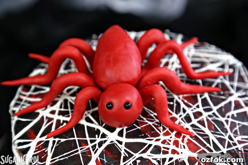 Red Velvet Marshmallow Spiderweb Cake—classic red velvet cake with black chocolate buttercream, covered with a web of marshmallow spiderwebs! Red Velvet Marshmallow Spiderweb Cake - close-up of red candy spider on top of cake