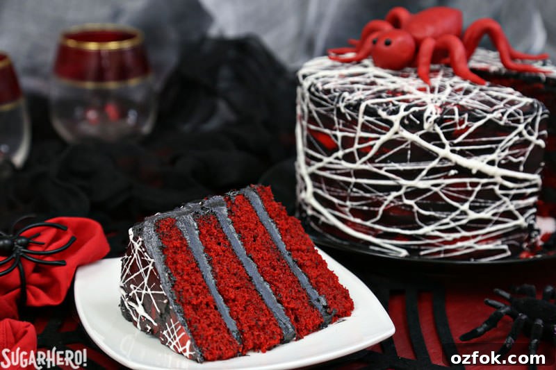 Red Velvet Marshmallow Spiderweb Cake—classic red velvet cake with black chocolate buttercream, covered with a web of marshmallow spiderwebs! Red Velvet Marshmallow Spiderweb Cake - slice of cake on a plate with full cake behind it