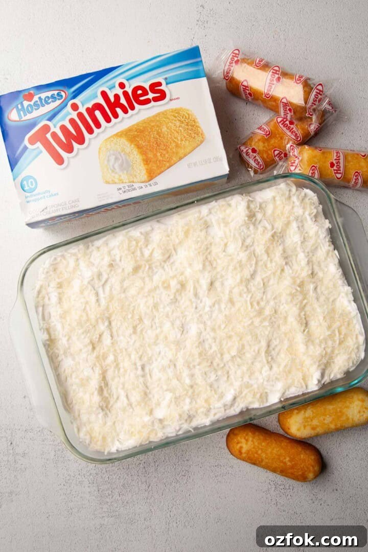 Creamy Twinkie Layer Cake Recipe You’ll Love 7 twinkie cake topped with coconut next to a box of Twinkies.