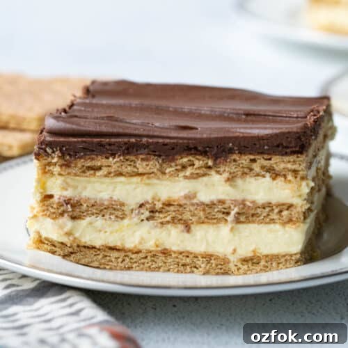 slice of layered chocolate eclair cake on a white plate, topped with chocolate frosting.