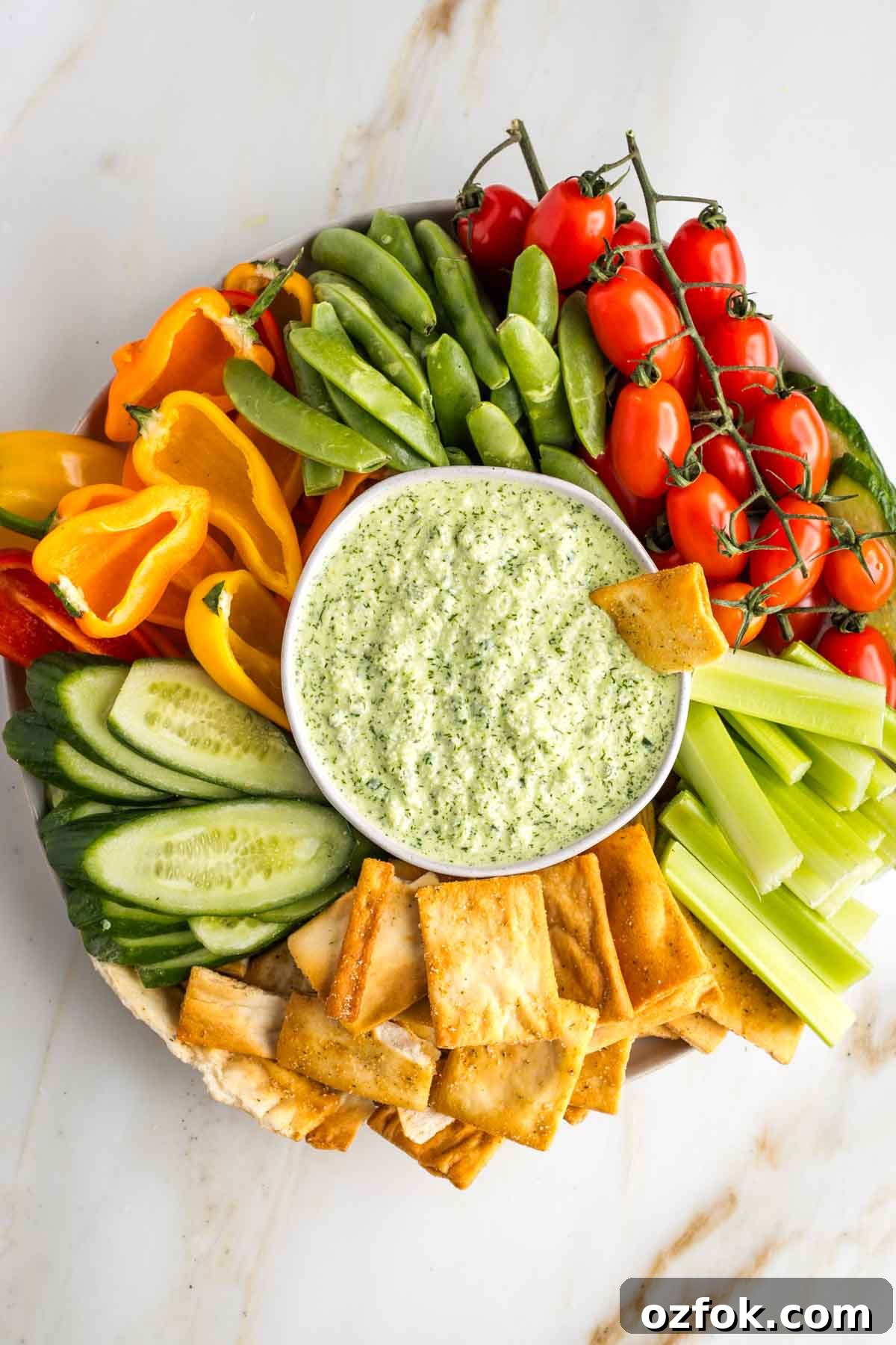 Dairy-Free Tzatziki Sauce: Authentic Vegan Greek Recipe 2 Green tzatziki dip in a bowl, surrounded by colorful veggies on a platter.
