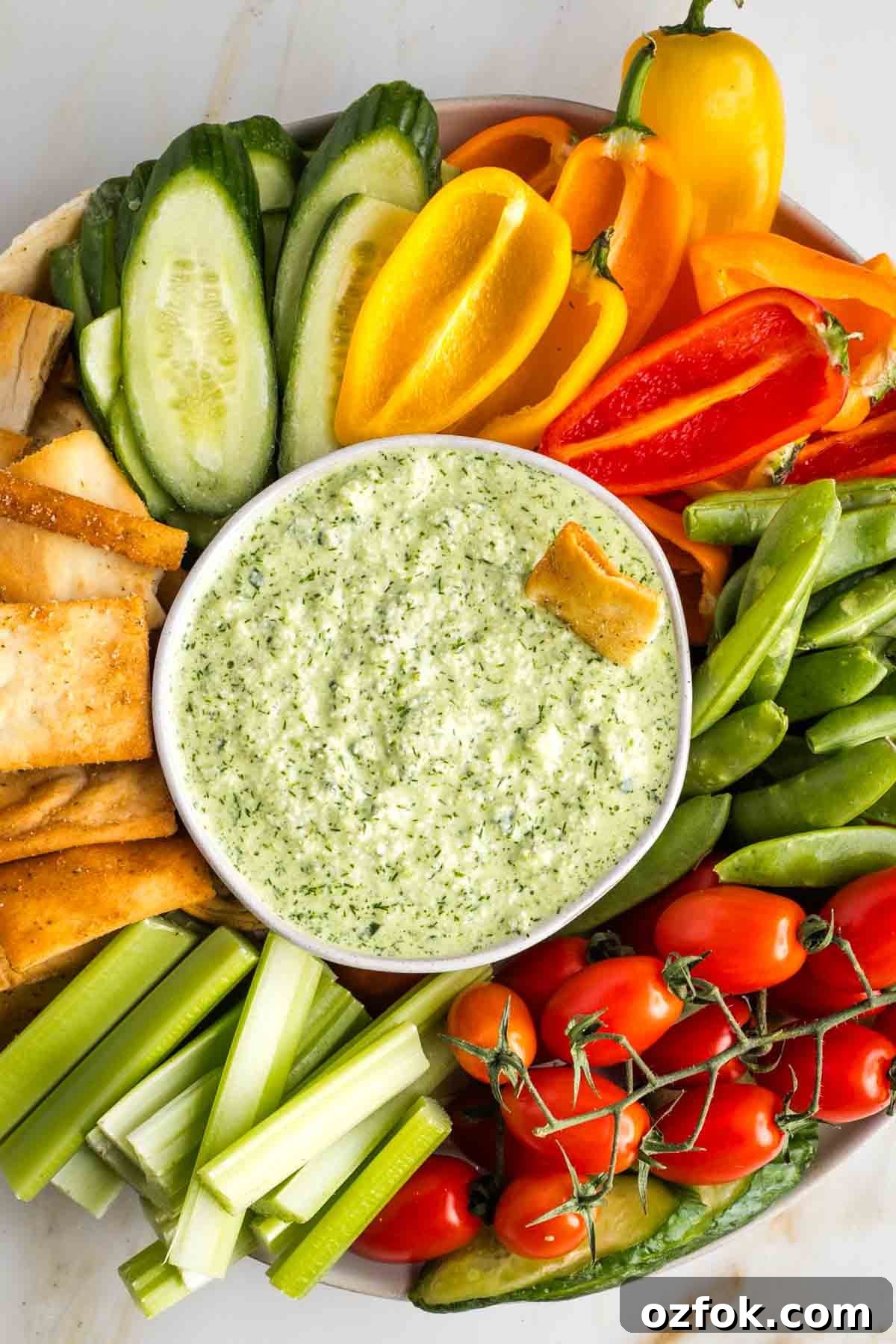 Dairy-Free Tzatziki Sauce: Authentic Vegan Greek Recipe 9 Dairy free tzatziki in a bowl surrounded by colorful vegetables and pita chips.