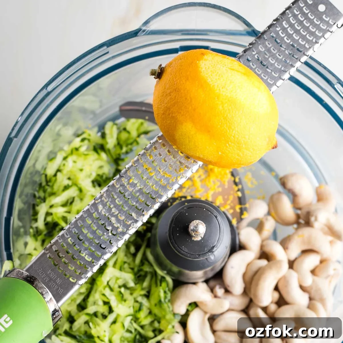 Dairy-Free Tzatziki Sauce: Authentic Vegan Greek Recipe 10 Zesting a lemon over a food processor filled with cashews and grated cucumber.