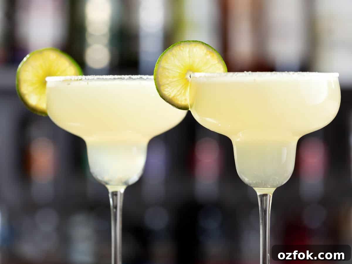 Guide to Cocktail Glasses: Styles, Uses, and Cocktail Pairings 9 A margarita glass with margarita and lime wheel on rim.