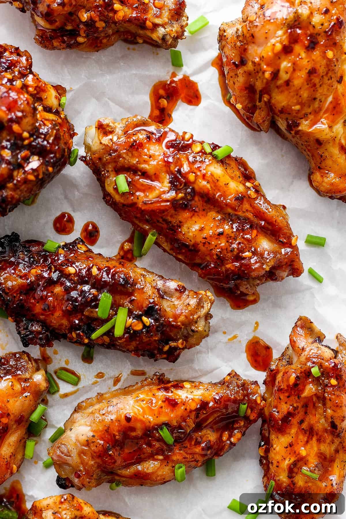 Honey Chili Crisp Grilled Chicken Wings Recipe 2 Glazed chicken wings sprinkled with sesame seeds and chopped green onions on parchment paper.