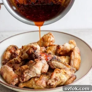 Honey Chili Crisp Grilled Chicken Wings Recipe 11 Pouring sauce over a plate of cooked chicken wings.