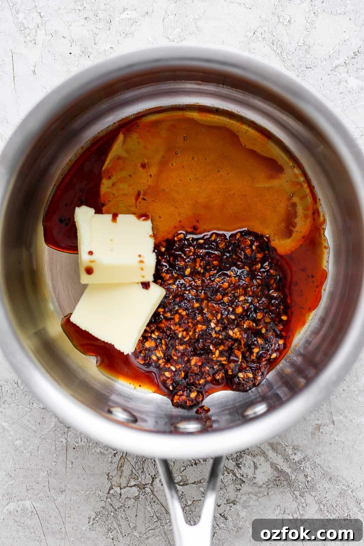 Honey Chili Crisp Grilled Chicken Wings Recipe 3 Ingredients in a saucepan including butter, chili flakes, and a dark liquid, possibly soy sauce or vinegar, preparing for a recipe.