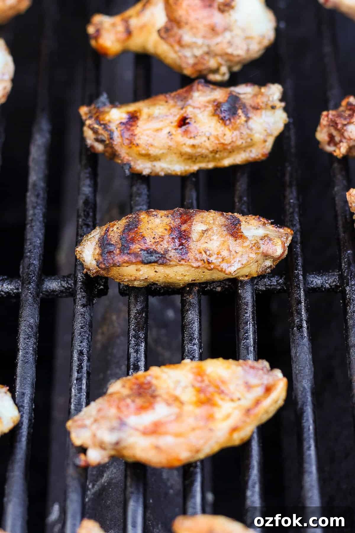 Honey Chili Crisp Grilled Chicken Wings Recipe 4 Grilled chicken wings on a barbecue grill with grill marks visible.