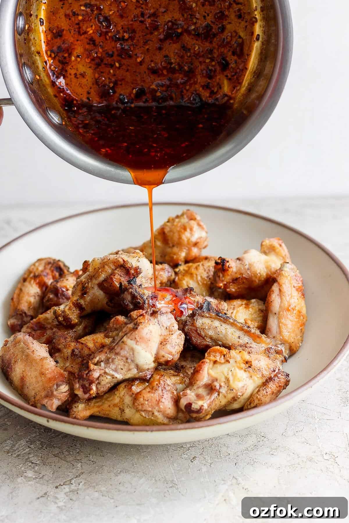 Honey Chili Crisp Grilled Chicken Wings Recipe 5 Pouring sauce over a plate of cooked chicken wings.