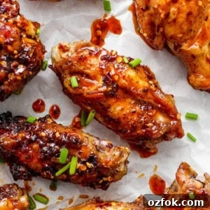 Honey Chili Crisp Grilled Chicken Wings Recipe 7 Glazed chicken wings on parchment paper garnished with sesame seeds and chopped green onions.