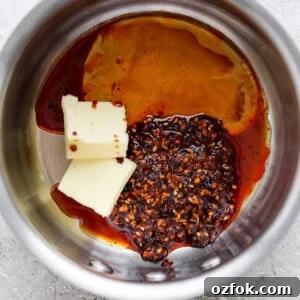 Honey Chili Crisp Grilled Chicken Wings Recipe 9 Ingredients in a saucepan including butter, chili flakes, and a dark liquid, possibly soy sauce or vinegar, preparing for a recipe.