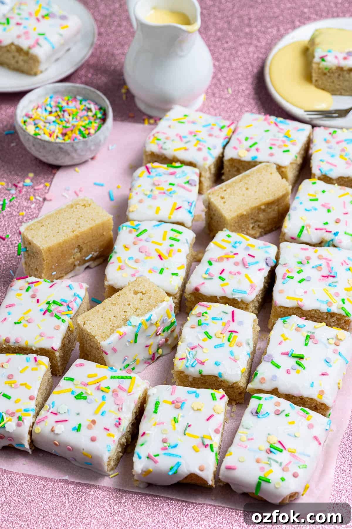 Vegan Birthday Cake Ideas for School Parties 4 Close up of vegan school cake on a pink background with a jug of custard and bowl of sprinkles.