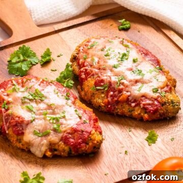 Keto Air Fryer Chicken Parmesan Recipe for Crispy Low-Carb Dinner 14 Two keto chicken parrmesan fillets on a cutting board with a tomato.