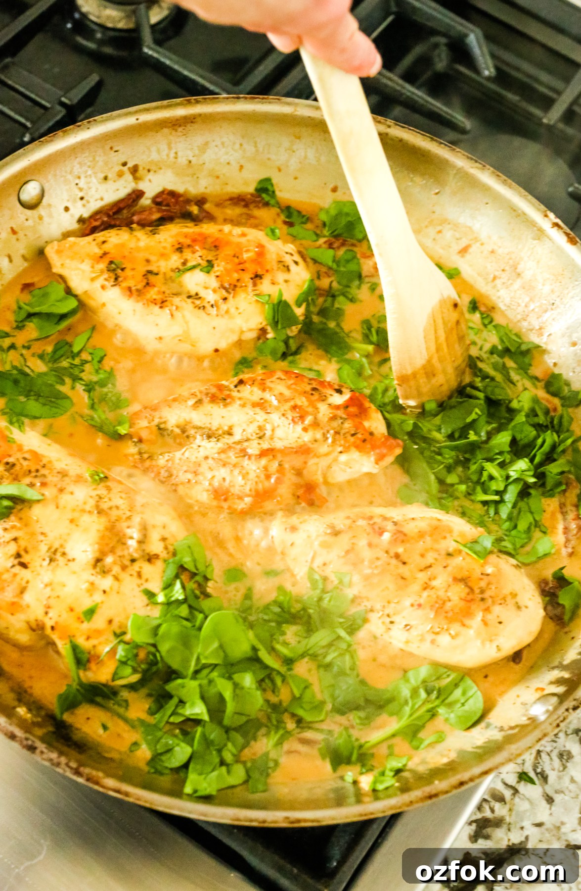 Tuscan-Style Dairy-Free Chicken with Sun-Dried Tomatoes and Herbs 7 stirring spinach leaves into sauce with chicken breasts