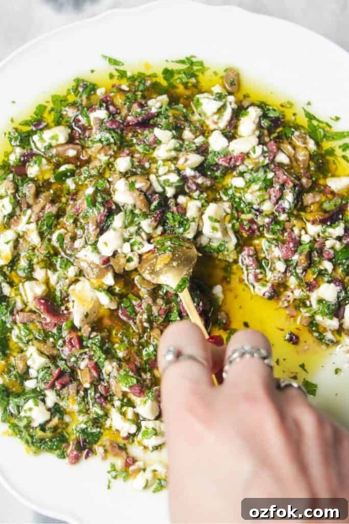 10-Minute Mediterranean Bread Dipping Oil Recipe 7 Hand mixing ingredients for Greek dipping oil in a large white plate.