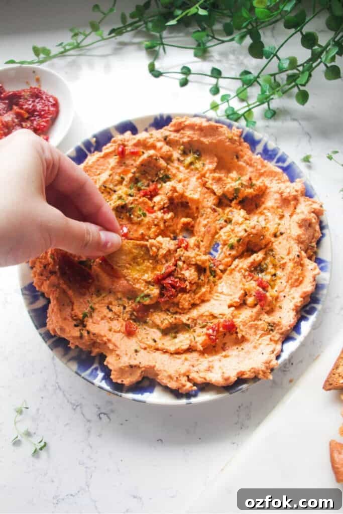 10-Minute Mediterranean Bread Dipping Oil Recipe 8 Hand dipping pita chip in sundried tomato feta dip on a small blue and white plate.
