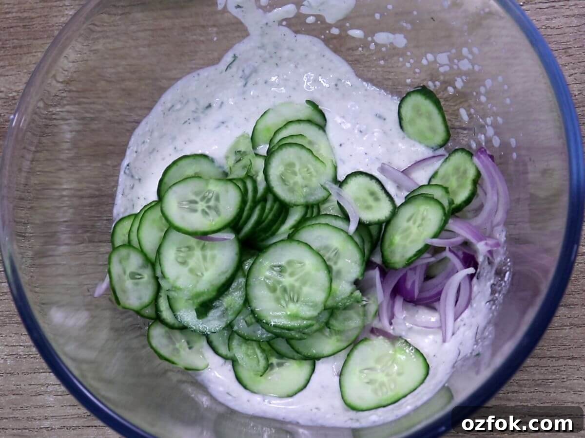 Creamy Greek Yogurt Cucumber Salad with Dill and Lemon 6 Mixing cucumber and red onion with Greek yogurt dressing in a bowl.