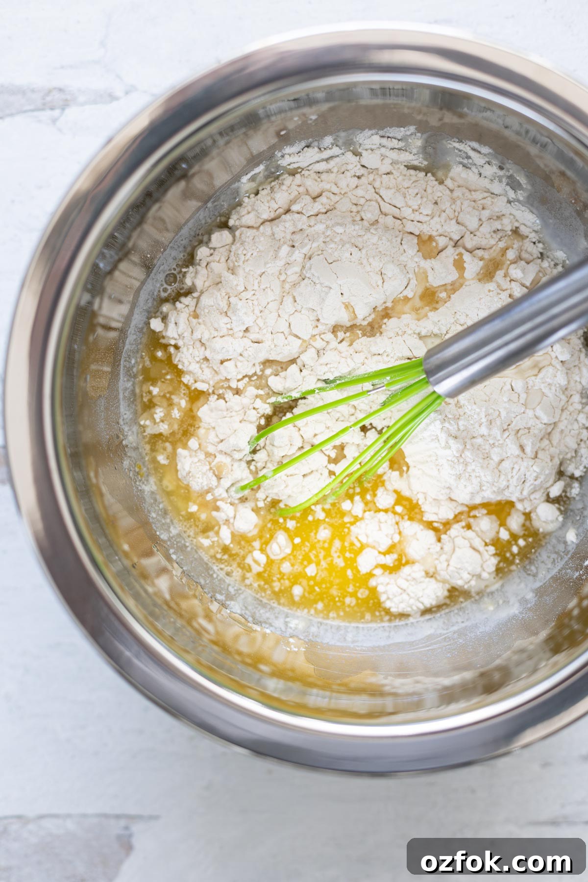 Silver mixing bowl of batter ingredients and a whisk.