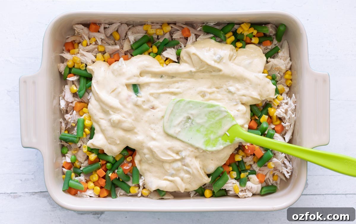 Pyrex pan of shredded chicken, mixed vegetables with sauce on top.