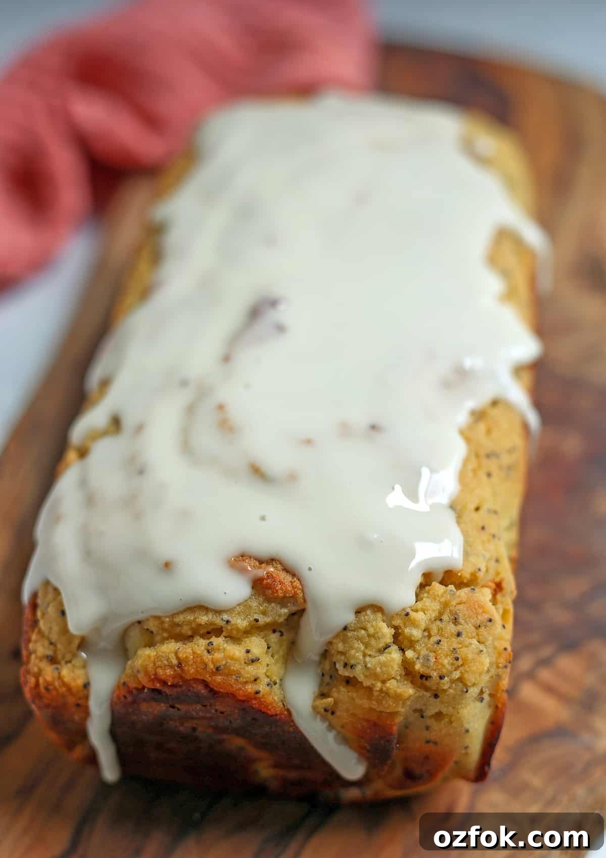 Paleo Lemon Poppy Seed Loaf — Gluten-Free Citrus Bread 5 A loaf of lemon poppy seed bread on a cutting board, the top covered in a glaze.