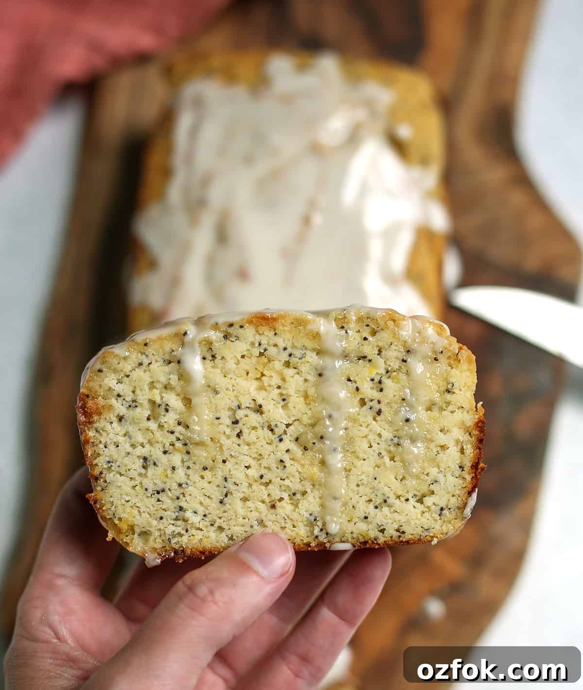 Paleo Lemon Poppy Seed Loaf — Gluten-Free Citrus Bread 6 A hand holding a slice of lemon poppy seed bread with glaze dripping down.