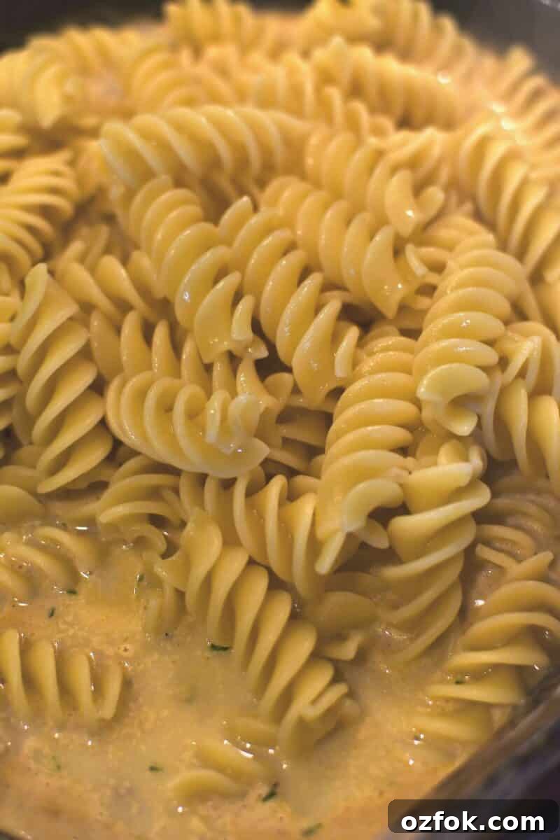 Adding the cooked pasta to the pan to be stirred into the sauce.