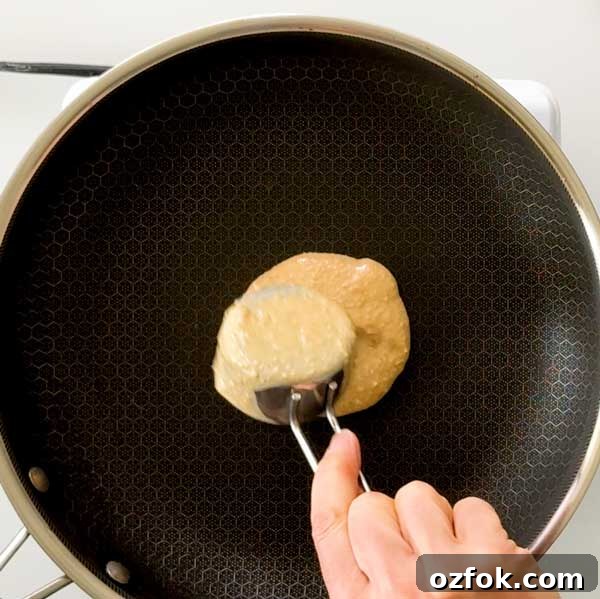 Fluffy Gluten-Free Oat Flour Protein Pancakes 7 Pouring the pancake batter into a skillet with a measuring cup.