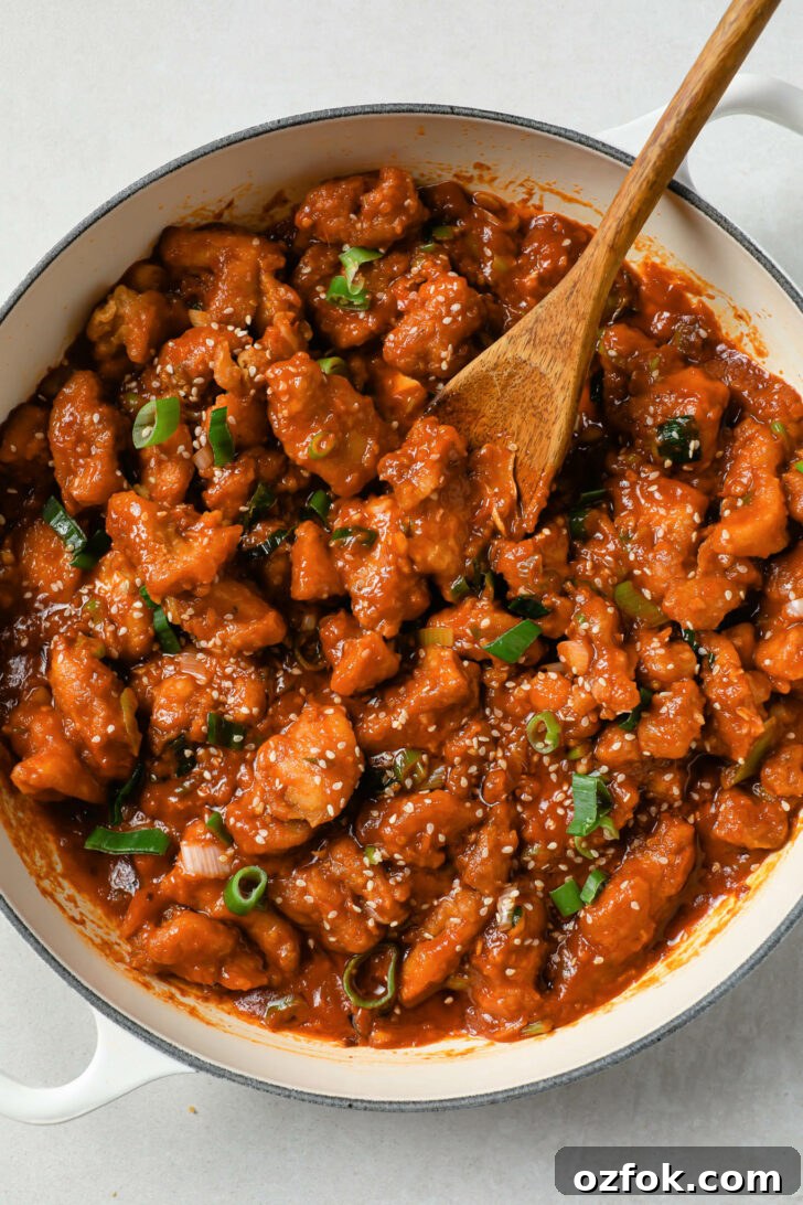 Crispy Chicken Manchurian with Tangy Gravy 2 Manchurian chicken in a pot with a wooden spoon and garnished with sesame seeds and green onion