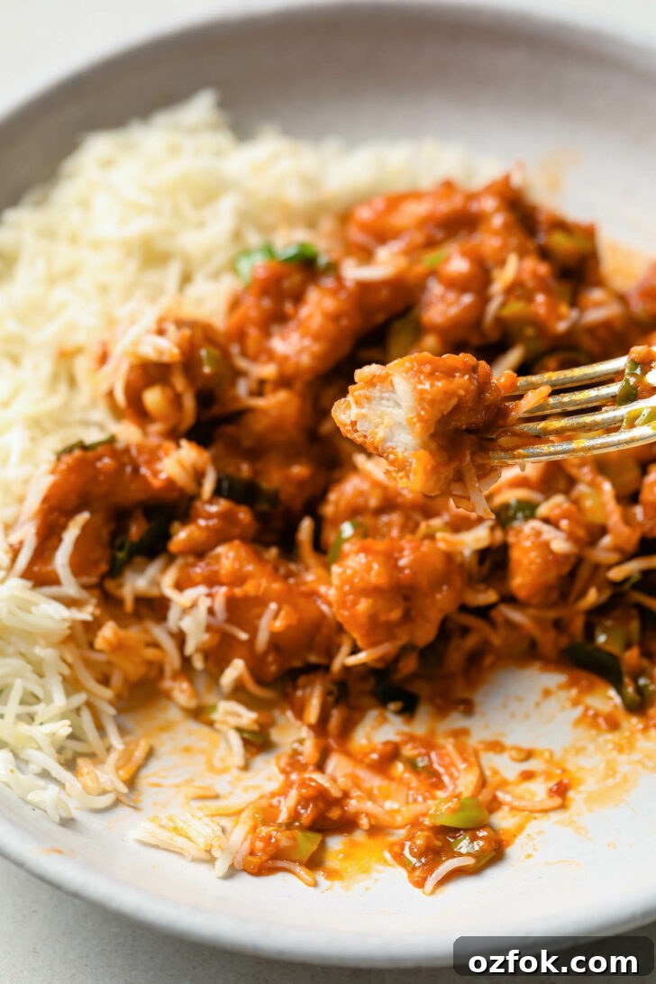 Crispy Chicken Manchurian with Tangy Gravy 5 Holding piece of chicken over a plate of partially eaten Chicken Manchurian with rice