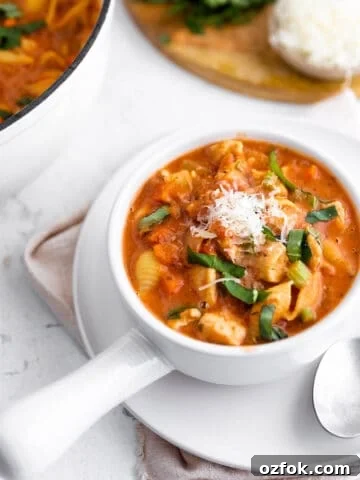 A handled soup bowl with a tomato soup with chicken, basil and parmesan.